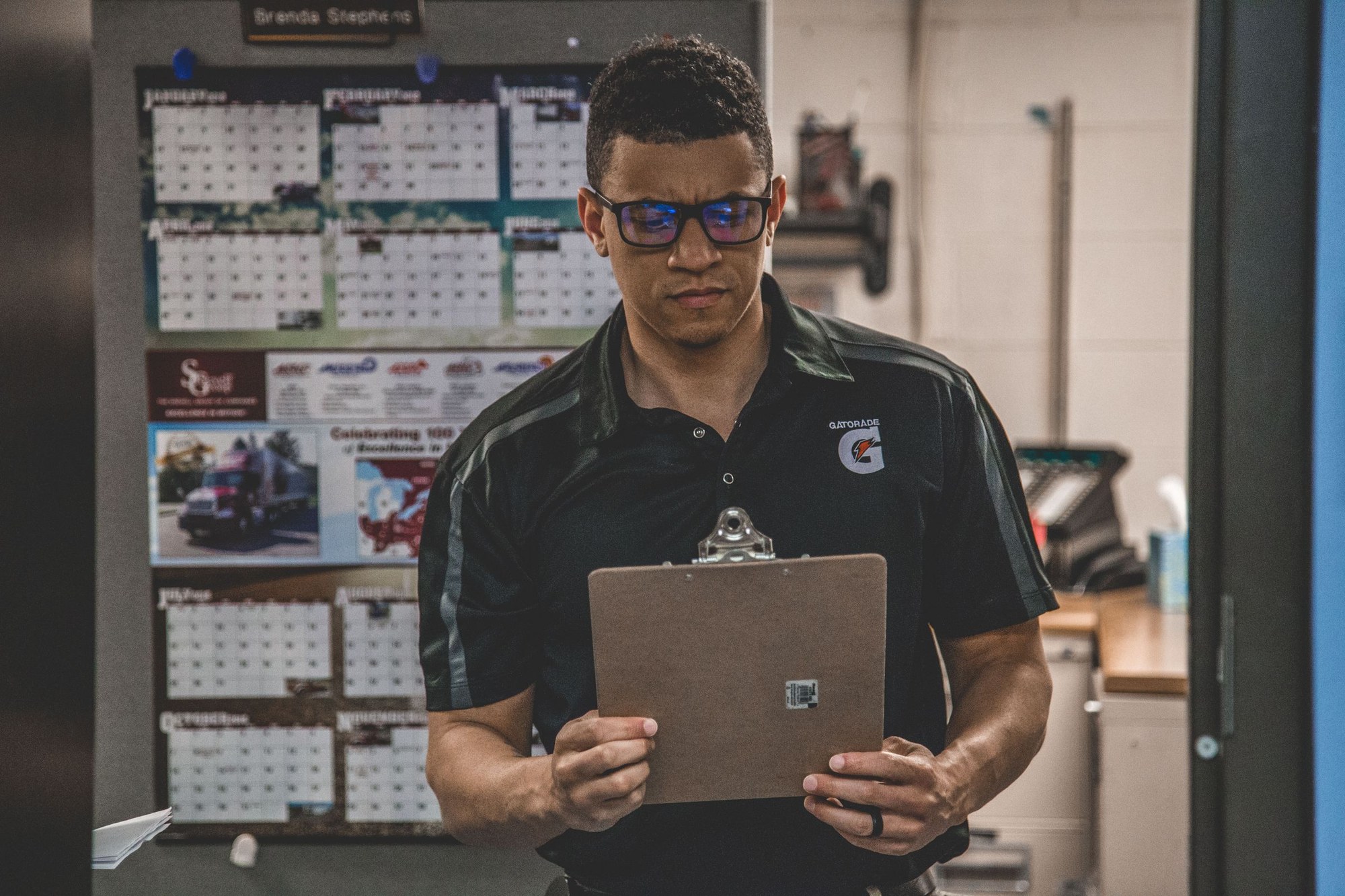 A logistics worker wearing glasses reviews paperwork on a clipboard.